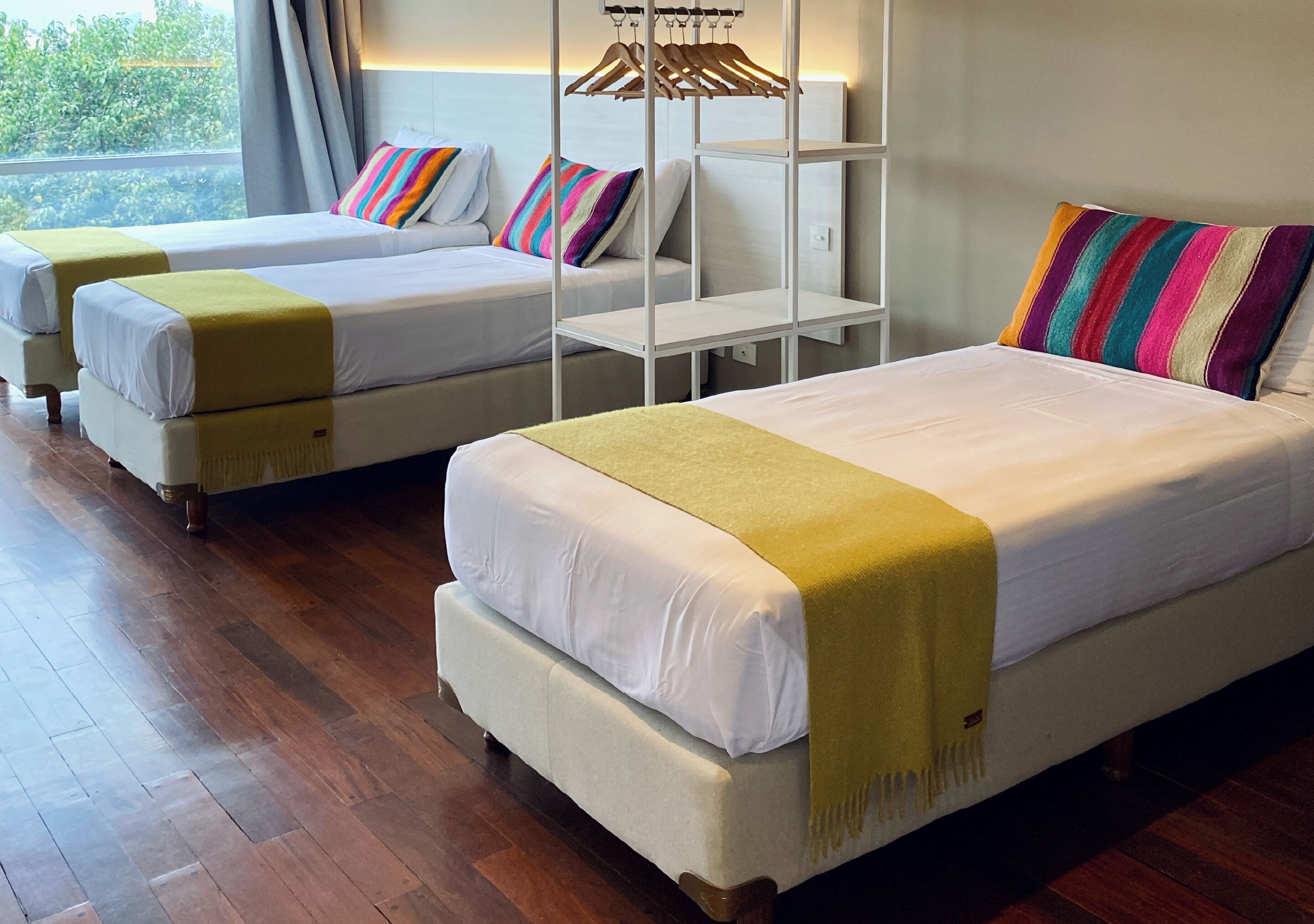 Habitación de hotel con dos camas, cada una con ropa de cama blanca y un plaid amarillo. Un perchero de madera está sujeto a la pared sobre las camas.