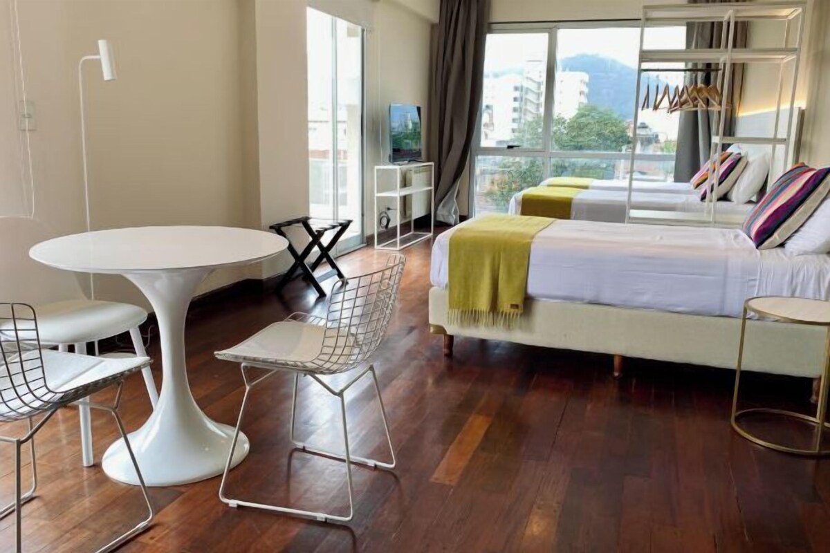 A modern hotel room with a large bed, a round dining table, and a white chair.
