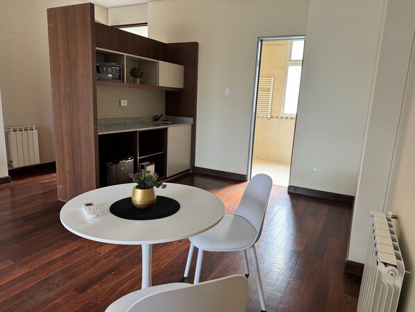 A modern kitchen with built-in appliances, a dining area with a round table and chairs, and a view of the outside. - Roomie Salta by DOT Suites (Salta)