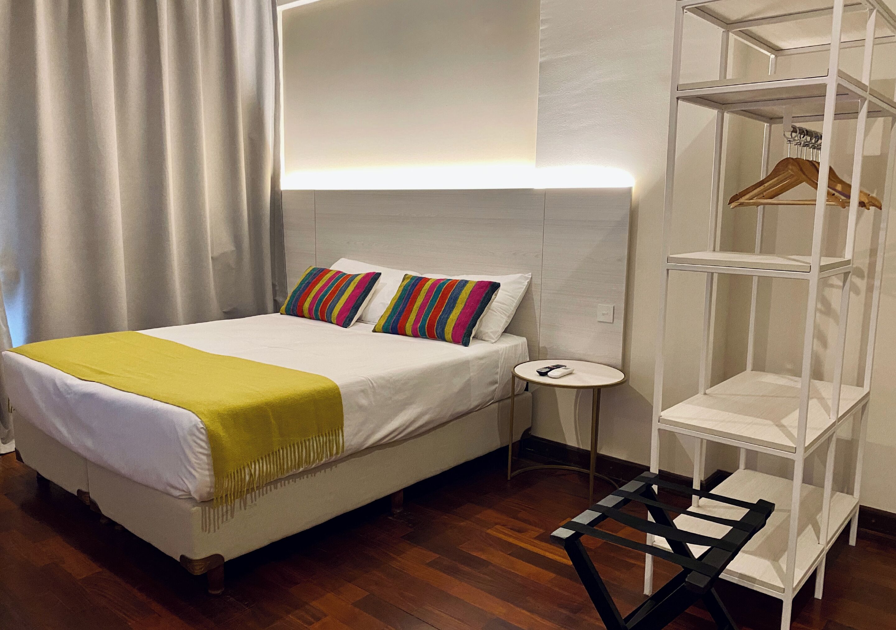 Un dormitorio ordenado con cama, mesita de noche y estantería blanca con perchero.