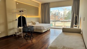 A hotel room with a bed, a seating area, a wardrobe, and a suitcase. - Roomie Salta by DOT Suites (Salta)