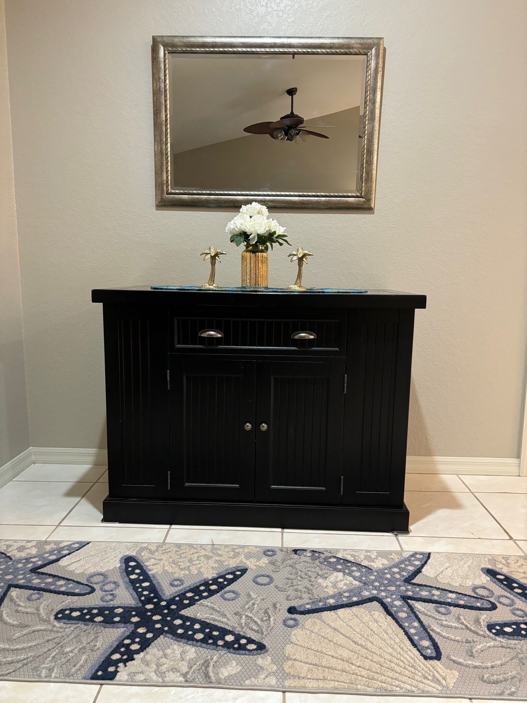 A black vanity with a mirror above it, a ceiling fan, and a starfish rug on the floor.