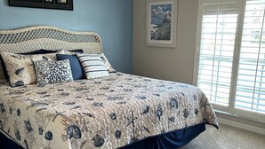 Une chambre à coucher avec un lit, un ventilateur de plafond, une fenêtre avec des stores et un tableau encadré au mur.
