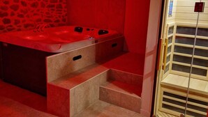 A spa room with a stone wall, a red-lit bathtub, and a wooden door with a window. - Gîte Bien-être Avec Jacuzzi & Sauna à la Campagne (Saint-Victurnien)