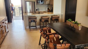 A spacious kitchen with a central island, stainless steel appliances, and a dining area with a dark table and leather chairs. - Welcome to Your Dream Getaway at Grand Solmar Pacific Dunes, Cabo! (Cabo San Lucas)