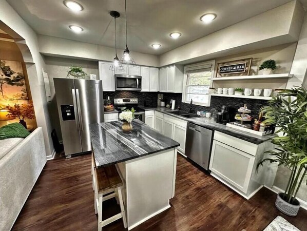 A modern kitchen with white cabinets, a stainless steel refrigerator, a microwave, and a coffee bar.