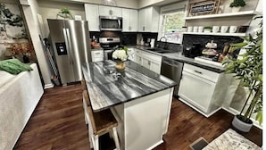 Una cocina moderna con armarios blancos, encimera de granito, electrodomésticos de acero inoxidable y una barra de café.