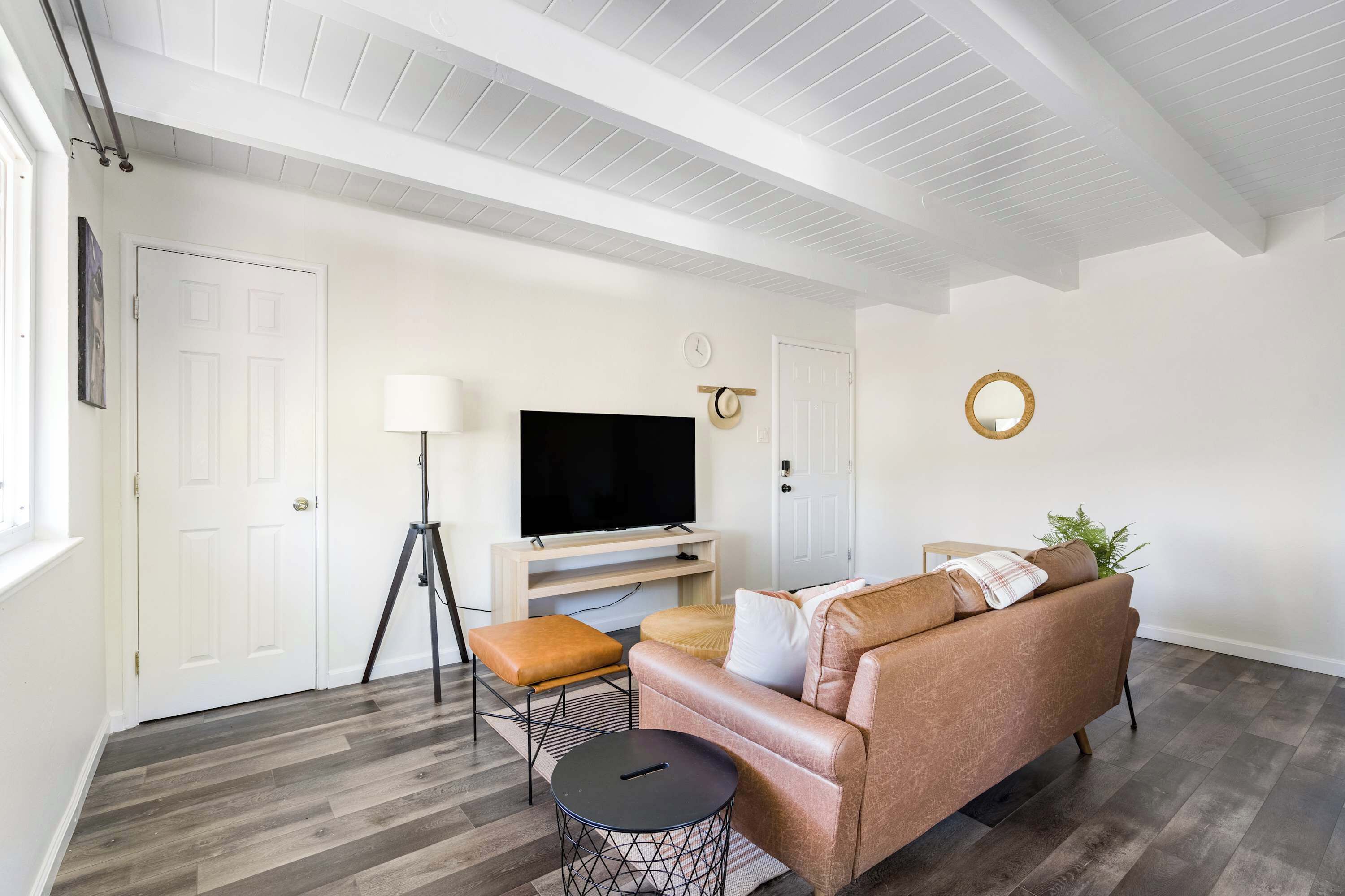 Un salon avec un canapé en cuir, un téléviseur posé sur un meuble, une lampe et un miroir rond accroché au mur.