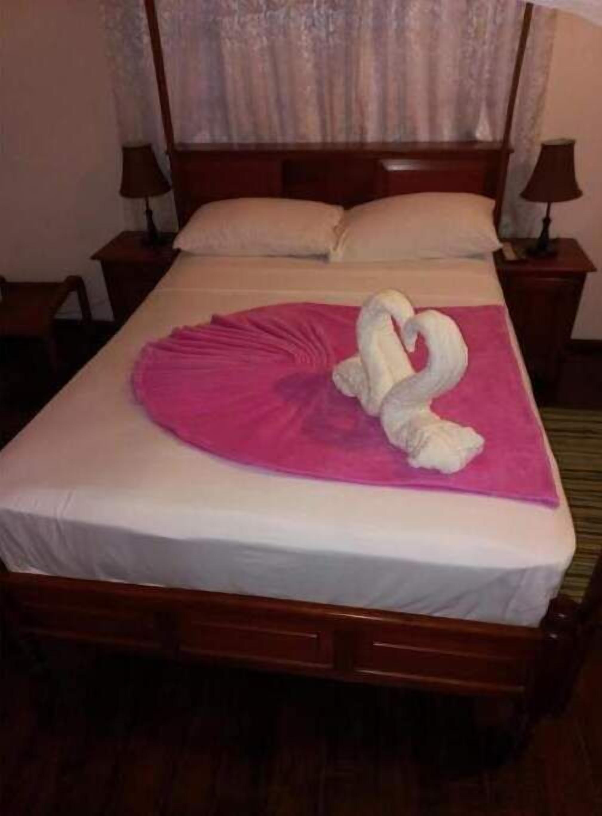 A neatly made bed with a pink towel and a white towel arranged in a swan shape.