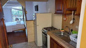 A compact kitchen with a gas stove, a refrigerator, and a sink. A television is mounted on the wall above the stove. - Castara Bliss Apartments B (Tobago)