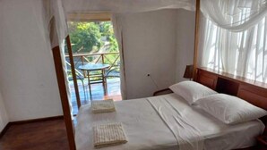A bedroom with a bed, a window with curtains, and a view of the outdoors. - Castara Bliss Apartments B (Tobago)