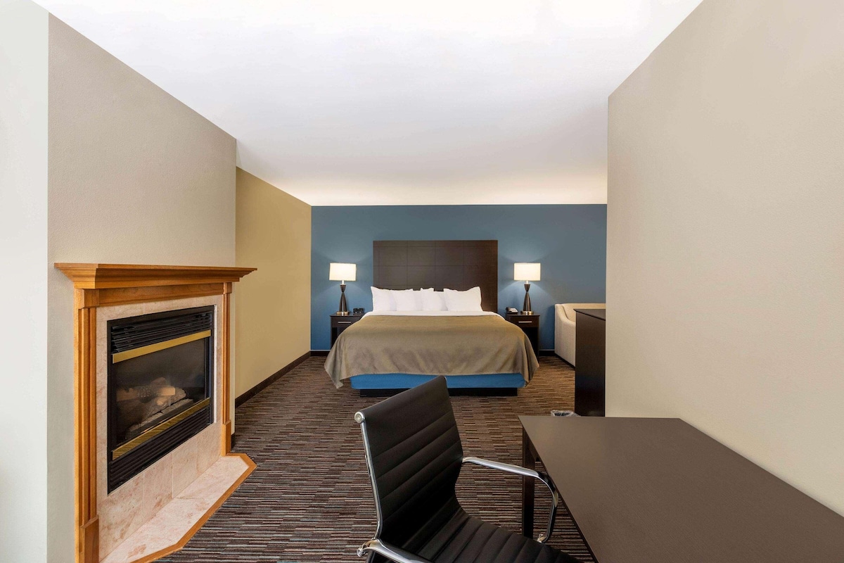 A hotel room with a bed, bedside lamps, a fireplace, and a desk.