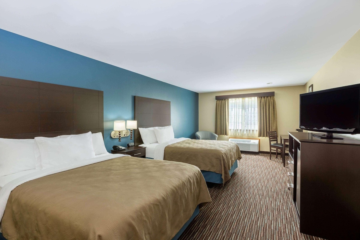 A hotel room with two beds, a television, a desk, and a chair.