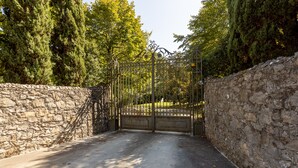 Un mur de pierre et un portail en métal mènent à une zone dallée.