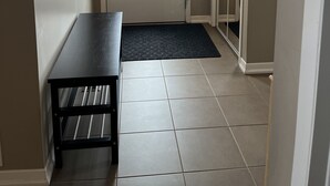A hallway with a door featuring a stained glass window, a bench, and a tiled floor.