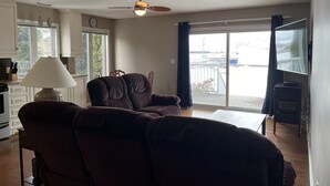 A living room with a sofa, a lamp, a ceiling fan, and a view of the outdoors through a sliding glass door.