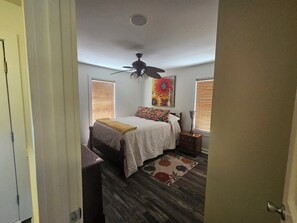 Un dormitorio con cama, mesita de noche, ventilador de techo y ventana con persianas.