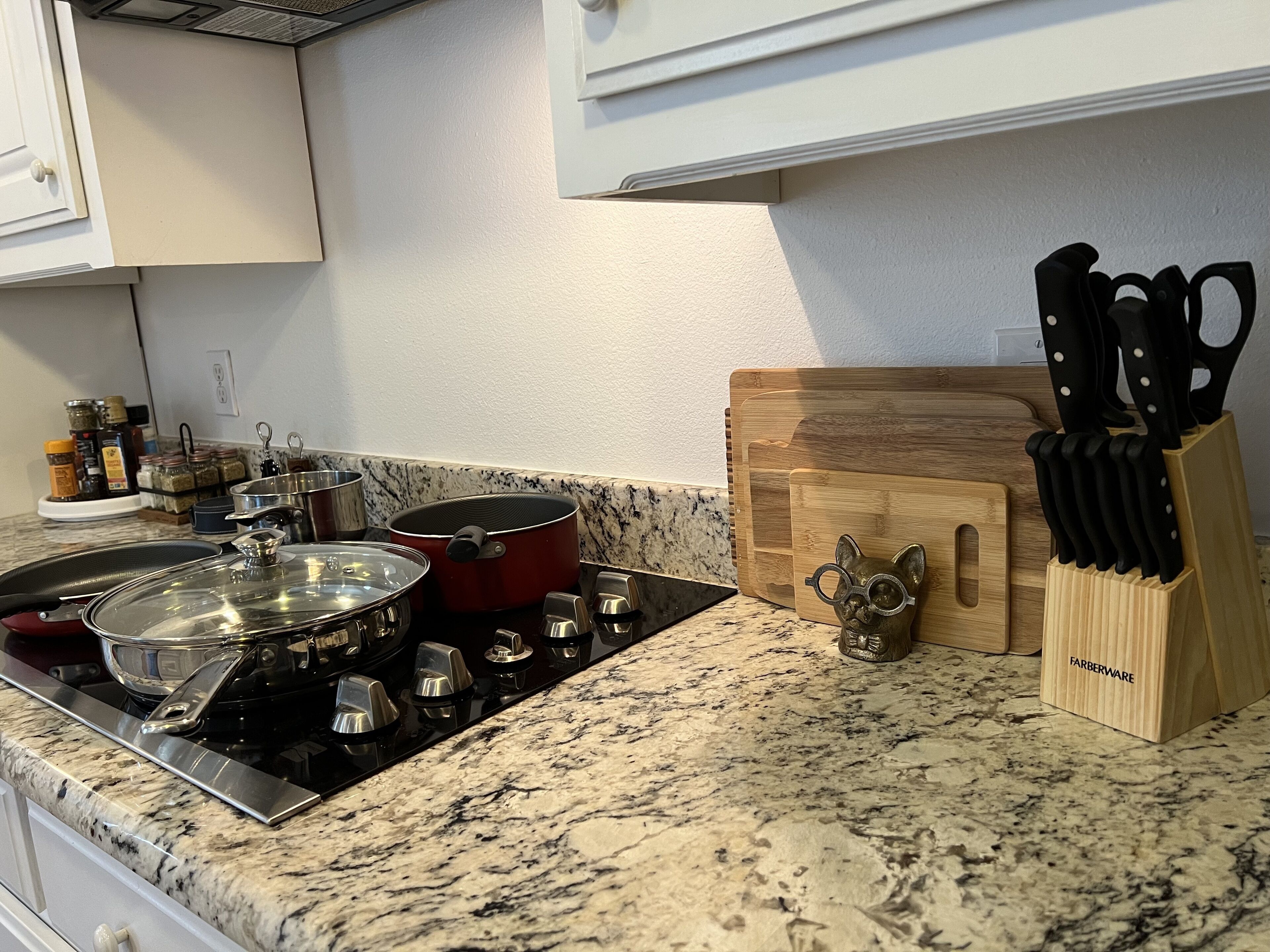 Una cocina con encimera de granito, estufa, olla roja, tabla de cortar de madera y bloque para cuchillos.