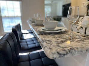 A dining area with a marble countertop, black leather chairs, and white tableware.