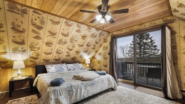 A bedroom with a large bed, two bedside lamps, a ceiling fan, and a view of the outdoors through a sliding glass door. - Charming Cottage on a hill by Camelback and Kalahari (Long Pond)