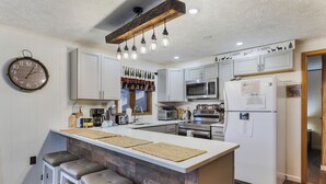 A modern kitchen with white cabinets, a large island with stools, a clock, and a wooden ceiling beam. - Charming Cottage on a hill by Camelback and Kalahari (Long Pond)