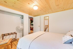 Ein Schlafzimmer mit Holzbalkendecke, einem Bett mit weißer Bettwäsche, einem Nachttisch, einem Stuhl, einem Ventilator und einem Spiegel an der Wand.