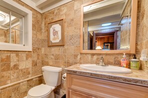 Ein Badezimmer mit Toilette, Waschbecken und Spiegel. An der Wand hängt ein gerahmtes Bild und über der Toilette befindet sich ein Fenster.