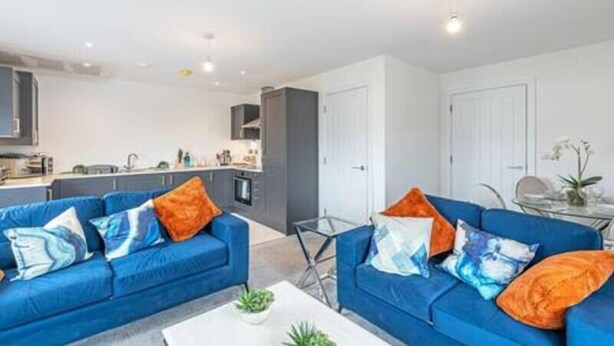 A modern living room with two blue sofas, a coffee table, and a kitchen area in the background. - Gospel Heights by Guestz (Heswall)