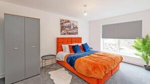 A bedroom with a bed, a wardrobe, a small table, a painting, a window with a view, and a plant. - Gospel Heights by Guestz (Heswall)