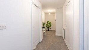 A narrow hallway with white walls and carpeted floor, leading to a room with a door at the end.