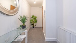 A narrow hallway with a glass vanity, a large mirror, and two potted plants.