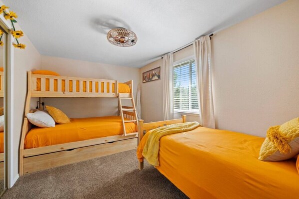 A room with two bunk beds, a ladder, a window with curtains, and a ceiling light fixture.