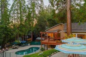A house with a pool, patio furniture, and a large tree.