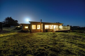 A modern house with large windows, a visible staircase, and a well-lit exterior at night. - Hansen's Bodega Bay Getaway-Walk to Beach! (Bodega Bay)