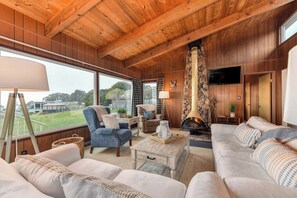 A cozy cabin interior with wooden walls, a fireplace, a television, and a large window offering a view of the outdoors.