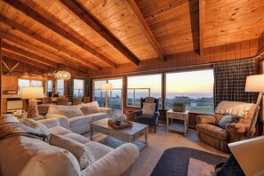 Un salon chaleureux avec un plafond haut, de grandes fenêtres et une vue sur le paysage.