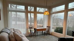 A cozy room with a sofa, a dining table, and chairs. Large windows offer a view of trees and a building outside. - Victorian Oasis home in Mineral City, near Atwood - Deer Hunting -  Hot Tub (Mineral City)