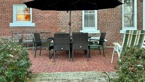 A patio with a table and chairs, a black umbrella, and a brick building with windows in the background. - Victorian Oasis home in Mineral City, near Atwood - Deer Hunting -  Hot Tub (Mineral City)