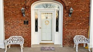 A brick building with a white door, two white benches, and a welcome mat. - Victorian Oasis home in Mineral City, near Atwood - Deer Hunting -  Hot Tub (Mineral City)