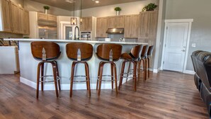 A modern kitchen with wooden cabinets, a central island with bar stools, and a stainless steel refrigerator. - Event Ready Spacious Tucson Villa w/ Private Pool (Tucson)