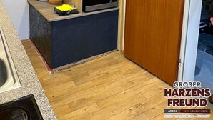 A compact kitchen with wooden shelves, a microwave, and a door leading to another room.