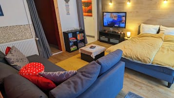 Ein modernes Wohnzimmer mit einer Couch, einem kleinen Tisch, einem Fernseher und einem Bett mit Kopfteil.