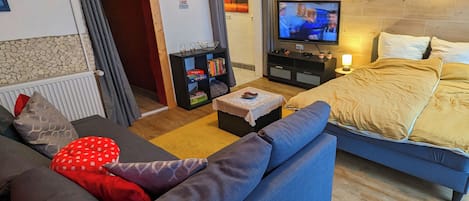 A modern living room with a sofa, a small table, a TV, and a bed with a headboard.