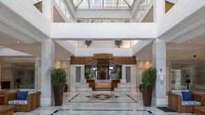 Eine großzügige Lobby mit einer zentralen Rezeption, großen Topfpflanzen und einem geometrisch gemusterten Boden.