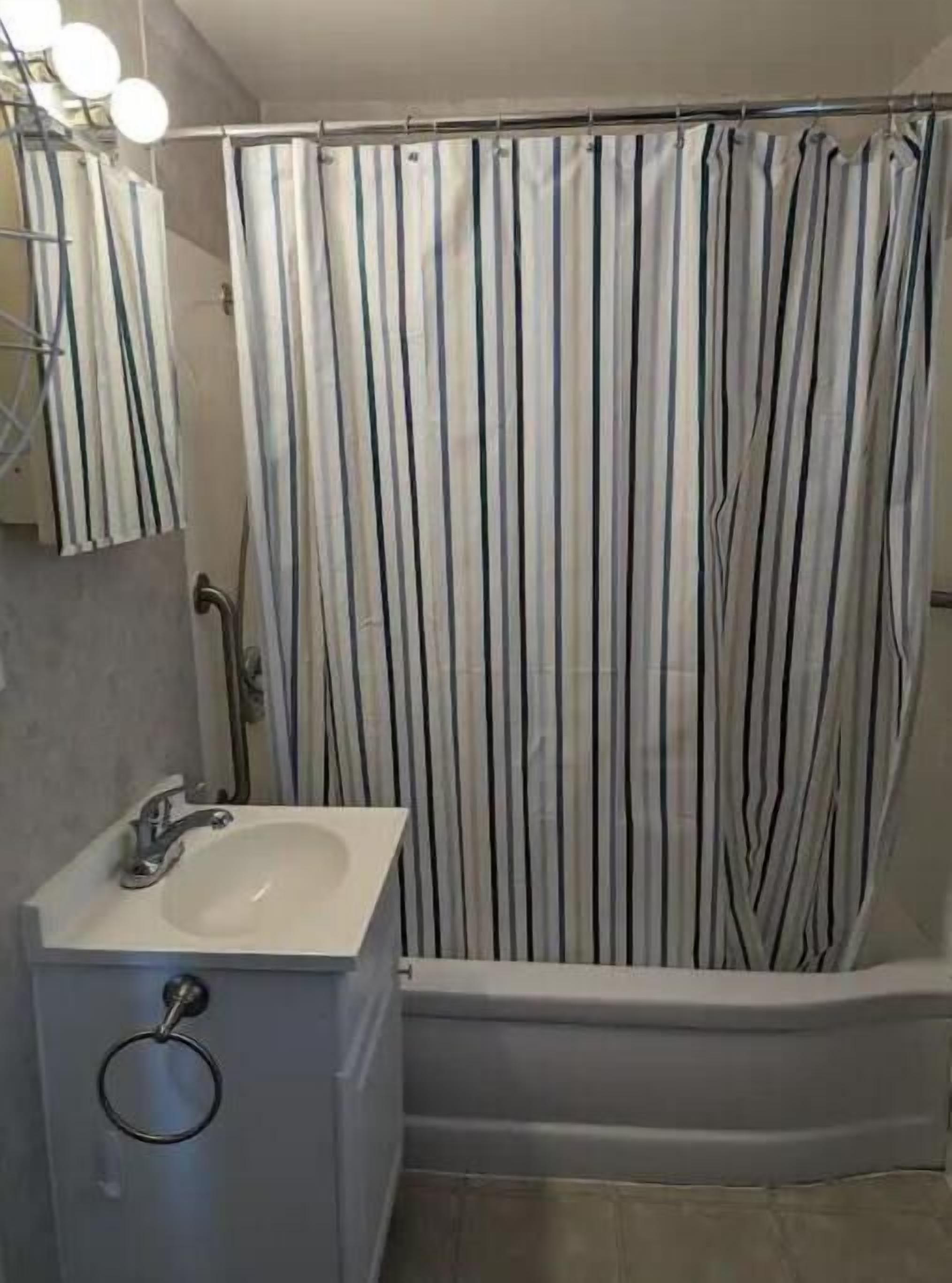 A bathroom with a shower curtain, a sink, and a mirror.