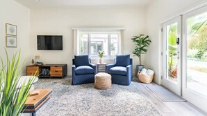 A modern living room with two blue armchairs, a wooden coffee table, a large window with a view of greenery, and a ceiling fan. - Private Guest House Central Location-Dog Friendly (Santa Barbara)