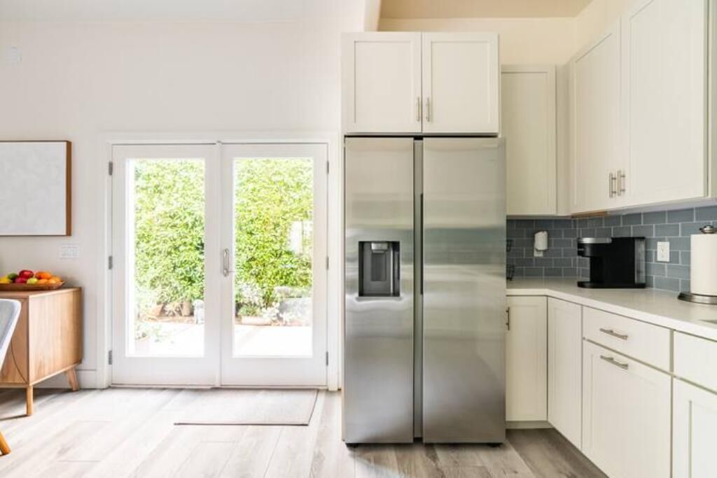 A modern kitchen with white cabinets, a stainless steel refrigerator, and a black coffee maker.