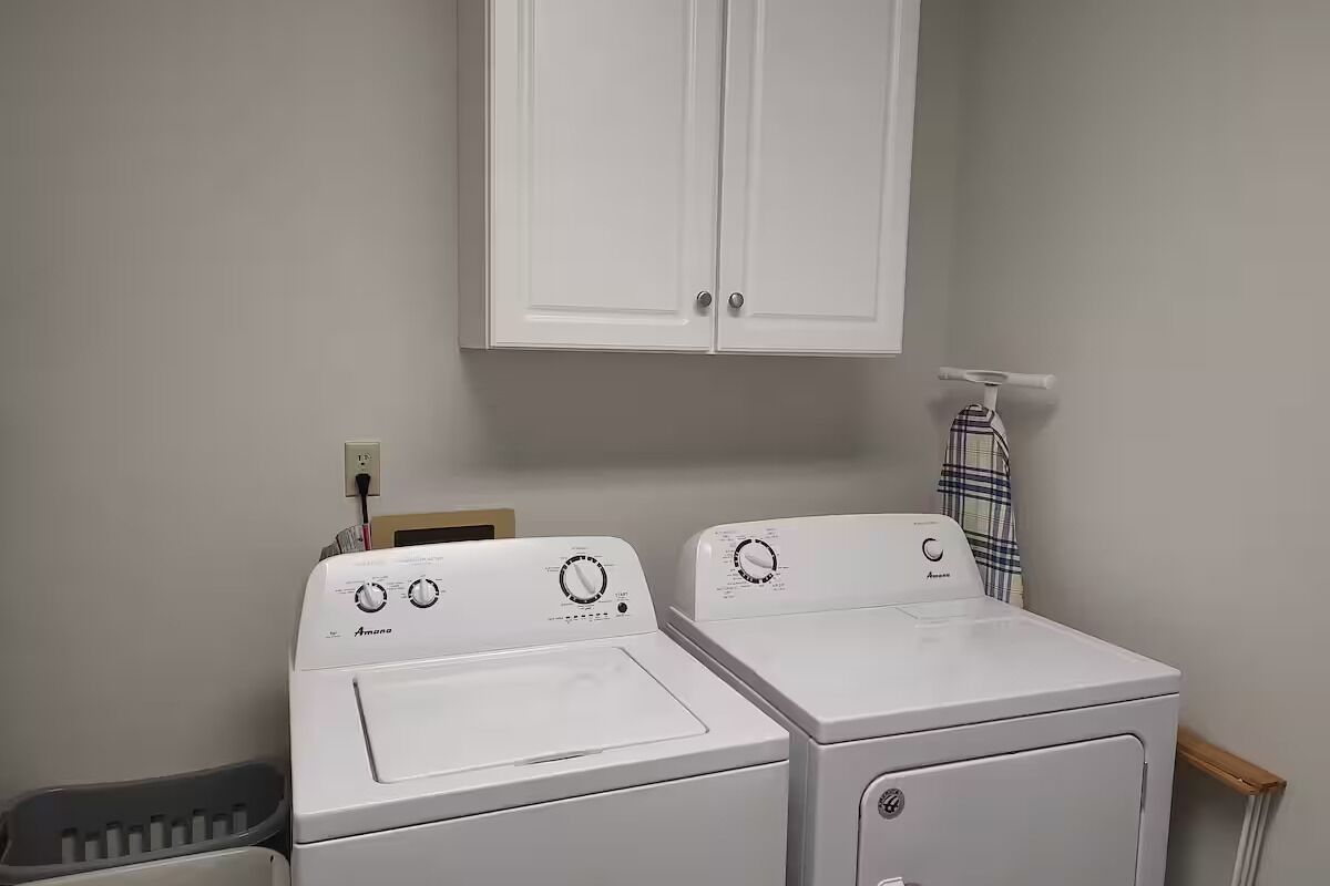 A laundry room with two front-loading washing machines and a white cabinet above.