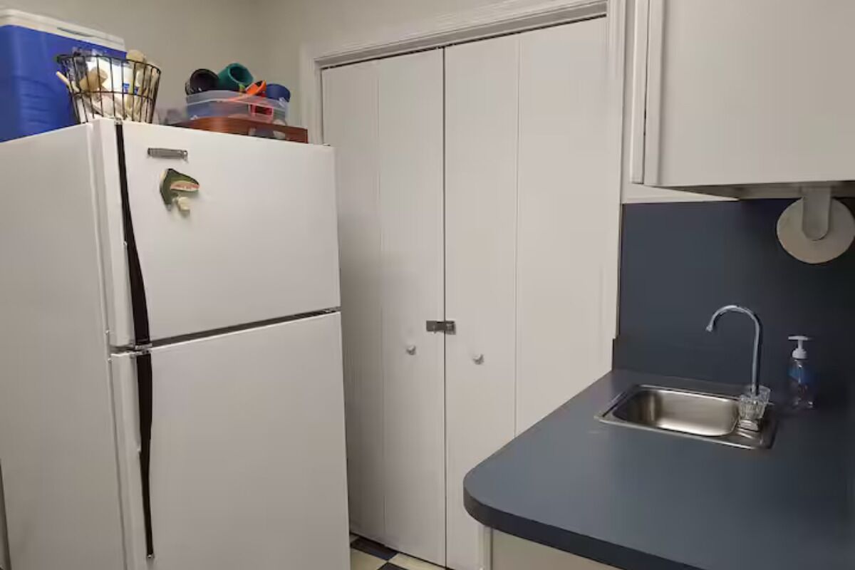 A compact kitchen with a white refrigerator, a built-in oven, a sink with a faucet, and cabinets.