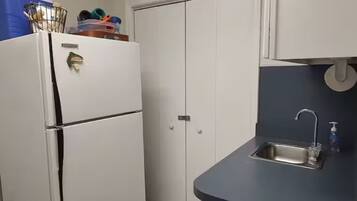 A compact kitchen with a white refrigerator, a built-in oven, a sink with a faucet, and cabinets.